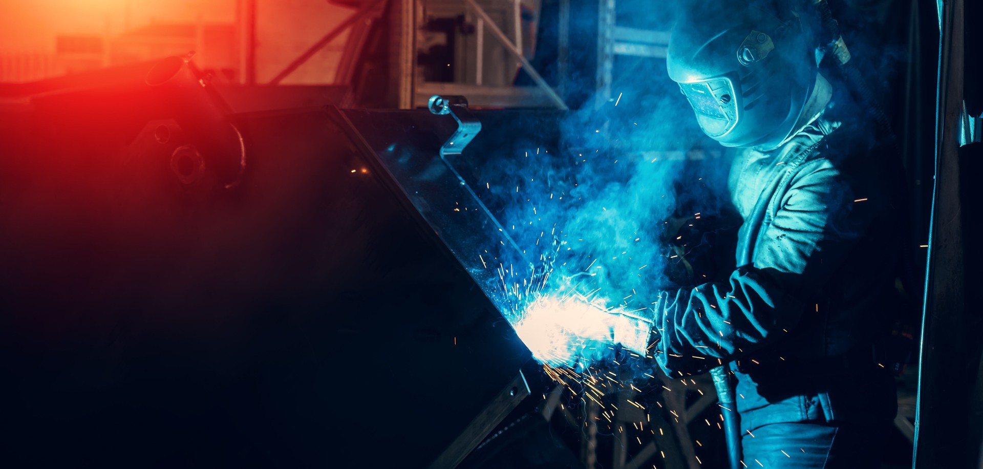 Industrial steel welder in process of work in metal factory. Sparks and smoke fly from welding