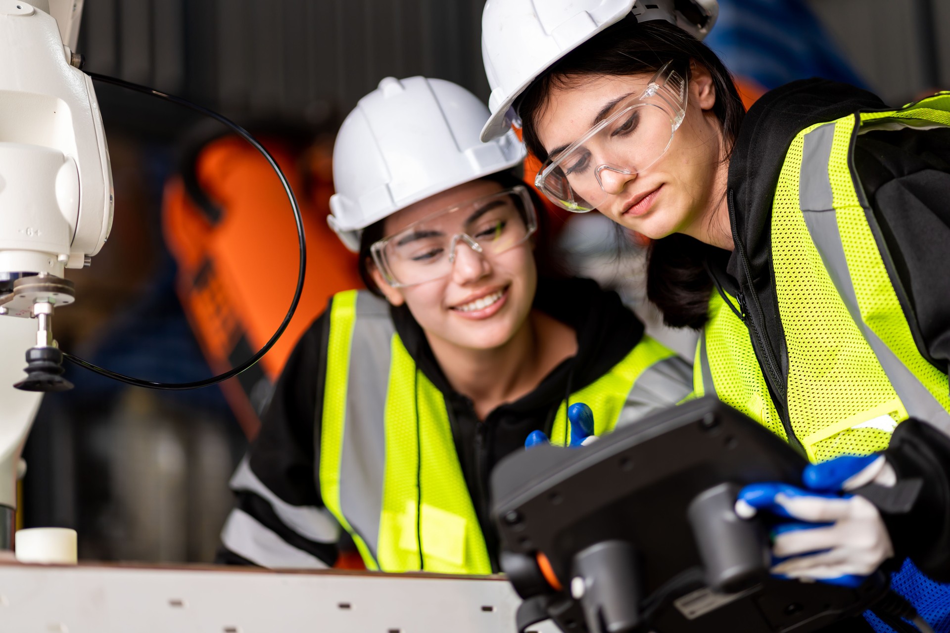 Un equipo de ingenieros masculinos y femeninos se reúnen para inspeccionar robots de soldadura de acero controlados por computadora. Planifique los ensayos y la instalación para su uso.